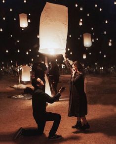 a man kneeling down next to a woman holding up a paper lantern in the air