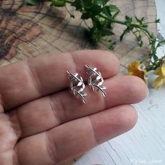 a person holding two tiny silver leaves on their fingers