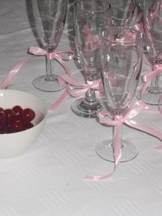 a bowl of cherries sits next to wine glasses on a table with pink ribbons