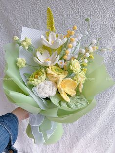 a bouquet of flowers sitting on top of a white cloth covered tablecloth with someone holding it in their hand