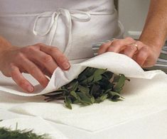 a woman in white apron preparing food on top of a cutting board with green vegetables