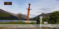 a large wooden cross sitting in the middle of a parking lot next to a lake