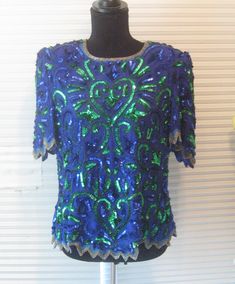 Stunning 1980s sequined beaded blouse. Royal blue and green. Made by Elegant Wear. Silk, lined. Has shoulder pads that can easily be cut out. Zigzag hems. Silver elongated beads at neckline and all edges. Zipper back. Great condition don't see any missing beads or sequins but cannot rule it out. Fits medium to large but please check your measurements. Bust 40" Length 24", 2 inches longer in back Shoulder to shoulder 16" FOR RETURNS YOU MUST MAIL BACK WITHIN 7 DAYS OF RECEIVING YOUR ORDER AND BUY Green Tops For Evening Party Season, Green Sequined Party Blouse, Blue Embellished Party Blouse, Fitted Blue Embellished Blouse, Fitted Green Top For Holiday, Fitted Green Top For The Holiday Season, Festive Blue Sequined Tops, Festive Green Sequined Tops, Festive Blue Sequin Tops