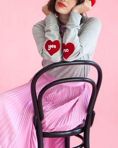 a woman sitting on top of a chair wearing a pink skirt and red hat with two hearts