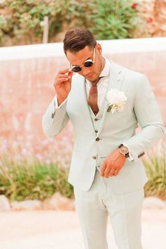 a man in a light blue suit and white flower boutonniere is looking at his watch