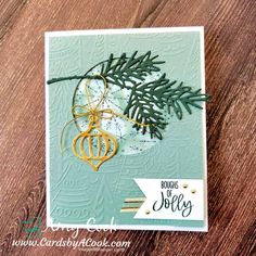 a close up of a christmas card on a wooden table with pine branches and ornaments