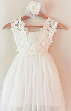 a white dress with flowers on it hanging from a hanger in front of a wall