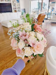 a person holding a bouquet of flowers in their hand on a wooden floor next to a couch