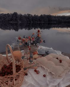 a picnic table is set up by the water with flowers and fruit in baskets on it