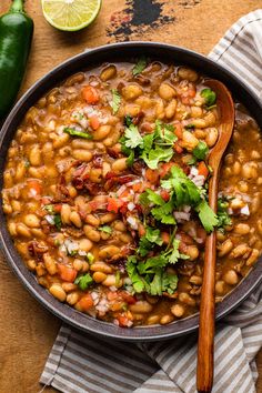 a bowl filled with beans and cilantro on top of a table next to a spoon