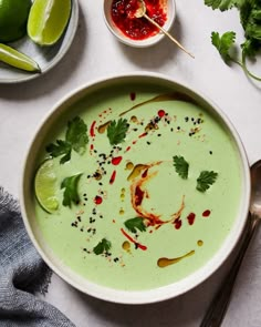 a white bowl filled with green soup next to limes and other condiments