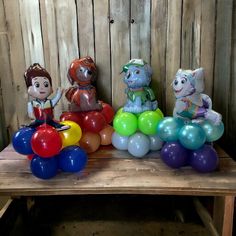 there are many balloons and toy figures on the table in front of the wooden fence