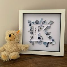 a teddy bear sitting next to a frame with scissors in the shape of a k