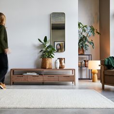 a woman walking through a living room with plants on the wall and a coffee table in front of her