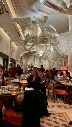 people sitting at tables in a restaurant with large sculptures hanging from the ceiling above them