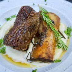 two pieces of steak on mashed potatoes and garnished with fresh herbs are served on a white plate