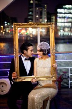 a man and woman sitting next to each other holding up a picture frame with the city lights in the background