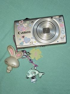 a digital camera sitting on top of a green surface next to a key chain and an animal charm