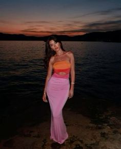 a woman standing on top of a beach next to the ocean at sunset with her dress blowing in the wind