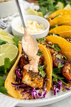 three fish tacos on a white plate with cole slaw and lime wedges