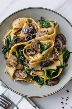 a white plate topped with pasta covered in mushrooms and spinach next to a fork