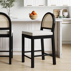 two black and white bar stools in front of a kitchen island with fruit on it