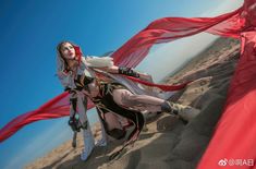 a woman dressed in white and black holding a red scarf on the sand at the beach