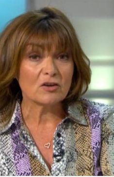 a woman with brown hair is sitting down and looking off to the side while wearing a snakeskin shirt