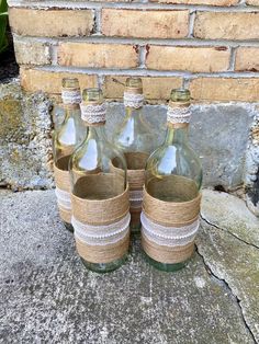 three empty glass bottles with twine rope wrapped around them sitting on the ground in front of a brick wall