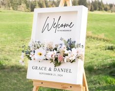 a welcome sign with flowers on it in front of a green field and grass area