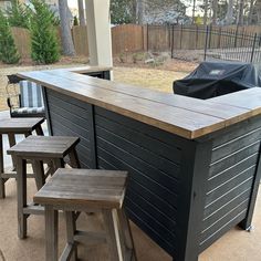 an outdoor bar with three stools and a grill in the back ground, on a patio