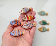 a hand is holding five colorful fish brooches in it's left palm