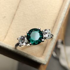 "A modern-styled engagement ring. It's a handmade 3-stone ring, set with an 8mm Emerald and two 5mm CZ accents. NOTE: ◊ This item is made to order, please allow 2-3 weeks for this ring to be handmade for you! Customizations and modifications are subject to longer production timelines and pricing. For rush orders, please contact me and we can discuss options :) ◊ For international orders please leaves your phone number in the \"note to seller\" at checkout for delivery purposes. ◊ Other stone opt Modern Three Stone Rings As Gift, Promise Three Stone Emerald Ring, Fine Jewelry Emerald Three Stone Promise Ring, Fine Jewelry Three Stone Emerald Ring For Promise, Fine Jewelry Three Stone Emerald Promise Ring, Elegant Three Stone Birthstone Ring, Elegant May Birthstone Ring With Three Stones, Three Stone Emerald Promise Ring, Elegant Three Stone Crystal Ring