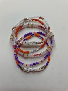 Set of five Clemson University handcrafted beaded bracelets celebrating college spirit! Each bracelet showcases vibrant school colors and is personalized with your college's name. Perfect accessory to flaunt your school pride or a thoughtful gift. Embrace your college journey with these stylish and meaningful bracelets! School Spirit Letter Beads Bracelets Gift, Personalized Orange Round Bead Jewelry, School Spirit Beaded Bracelets With Letter Beads For Gifts, School Spirit Beaded Bracelet With Letter Beads As Gift, Personalized Orange Beaded Bracelets As Gift, School Spirit Jewelry With Letter Beads For Gifts, Personalized Orange Beaded Bracelets For Friendship, Personalized Orange Bracelets With Round Beads, Meaningful Bracelets