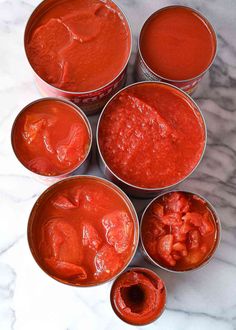 six tins filled with red sauce sitting on top of a marble countertop next to each other