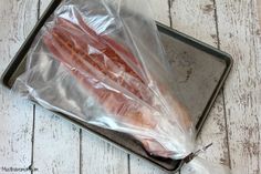 bacon wrapped in plastic sitting on top of a metal tray next to an empty bag