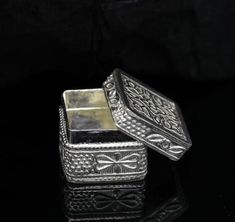 two silver boxes sitting side by side on a black surface, one is empty and the other has a bow