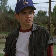 a young man wearing a baseball cap standing in front of a fence