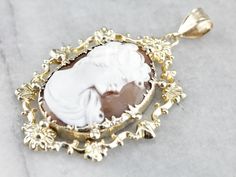 This vintage pendant features bright yellow gold flowers atop of the ornate decorative frame. The cameo at the center is a pretty, dark tan with bright white highlights in the portrait. Size to be noticed this is a fantastic statement piece! This pendant does not come with the chain shown. Please feel free to contact us, we will help you find the perfect chain for your style and budget! Metal: 14K Yellow Gold Gem: Shell Cameo Gem Measurements: 29.3 x 20.3 mm, Oval Measurements: 37 x 59 mm, with Luxury Yellow Gold Cameo Necklace, Luxury Cameo Yellow Gold Necklace, White Highlights, Decorative Frame, Cameo Ring, Vintage Cameo, Cameo Pendant, Vintage Pendant, Dark Tan