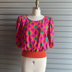 Bright floral silk in Orange pink and green. Has a knit band at waist and sleeves. Has moderate shoulder pads and puffy sleeves. Tags: Emmanuel Ungaro / size 12  100% Silk/ Fabric made in Italy Nice condition, no flaws c1980s also have a lime green with navy and red flowers Measures / meant to be worn loose shoulders 15" Bust 40" Waist Band (stretchy) up to 30" + Length 21 1/2" Vintage Pink Puff Sleeve Top, Multicolor Fitted Blouse With Balloon Sleeves, Fitted Multicolor Blouse With Balloon Sleeves, Fitted Multicolor Balloon Sleeve Blouse, Pink Fitted Blouse With Balloon Sleeves, Pink Fitted Blouse With Blouson Sleeves, Multicolor Fitted Blouse With Puff Sleeves, Fitted Multicolor Puff Sleeve Blouse, Pink Chiffon Dress