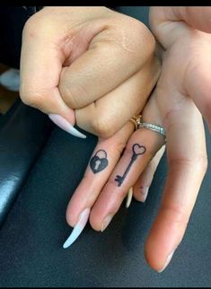 two people holding hands with tattoos on their fingers and one has a key tattoo on it