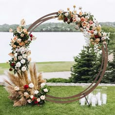 a wedding arch with flowers and candles on the grass next to water in the background