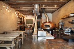 an industrial kitchen with wooden tables and stools in front of a large wood burning oven