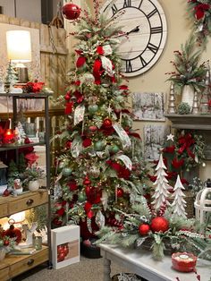 a christmas tree with red and green decorations in front of a large clock on the wall