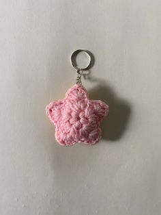 a pink crocheted star shaped keychain hanging from a hook on a white surface