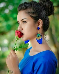 a woman holding a red rose in her mouth and wearing earrings on top of it