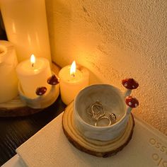 two wedding rings sit in a bowl on a table next to candles and napkins