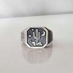 Custom Cactus Ring in Western Style: This oxidized 925 sterling silver ring is a unique piece that reflects the spirit of Western style and the Arizona valley. With its black background, the details on the front of the ring bring together the wild beauty of the desert and the symbols of Western culture. The bull skull, cactus, crescent moon, cowboy hat, and stars represent the unique features of Arizona, while the engraving of Monument Valley on the inside of the ring pays homage to the iconic l Western Ring, Aztec Rings, Skull Cactus, Cactus Ring, Western Rings, Cool Rings For Men, Chapeau Cowboy, Western Culture, Dad Fashion