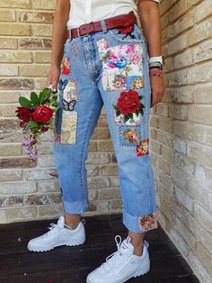 a woman standing in front of a brick wall with flowers and patches on her jeans