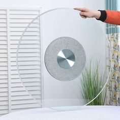 a person holding a circular glass object in front of a white bed with blue curtains